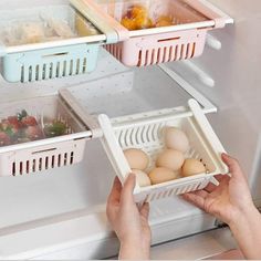 two hands holding trays filled with eggs in front of an open refrigerator freezer