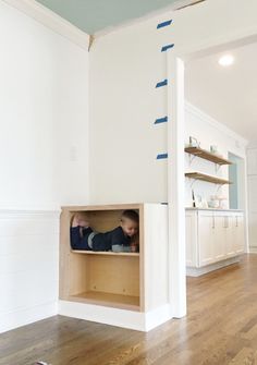 a young child is playing in the kitchen under an unfinished shelf with blue tape on it