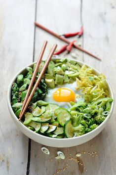 a white bowl filled with vegetables and an egg on top of it next to chopsticks