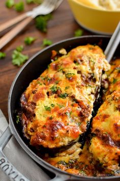 an omelet with meat and cheese in a pan on a wooden table next to utensils