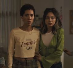 two young women standing next to each other in a living room, one is wearing a sweater that says feminine lead