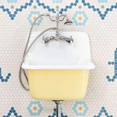 a yellow and white sink sitting on top of a metal stand in front of a tiled wall