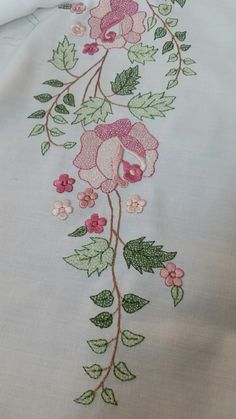 a white table cloth with pink flowers and green leaves on the edge, embroidered onto it