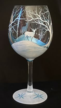 a wine glass with a deer and snow scene on the bottom, sitting on a black surface