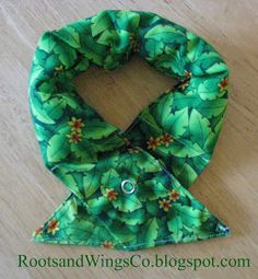 a green scarf with leaves on it sitting on top of a wooden floor next to a pair of scissors