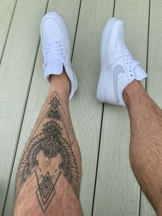 a man with a tattoo on his leg wearing white tennis shoes and blue shorts is standing on a wooden deck