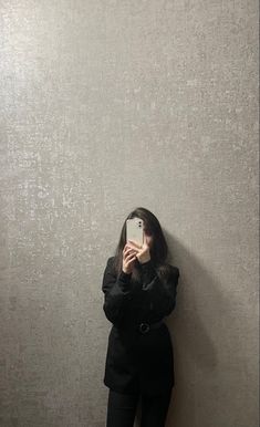 a woman standing in front of a wall taking a selfie with her cell phone