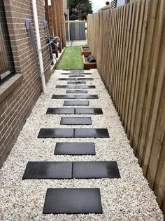 a walkway made out of stepping stones in front of a brick wall and wooden fence