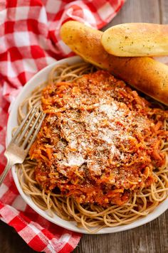 a plate of spaghetti with bread on the side and a red checkered table cloth