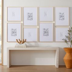 a white table sitting in front of a bunch of framed pictures on a wall next to a potted plant