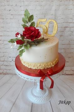 a white cake with red flowers and gold numbers on top, sitting on a table