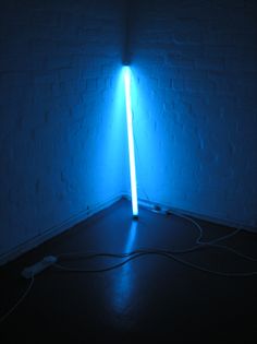 a blue light in a dark room with a white brick wall and black flooring