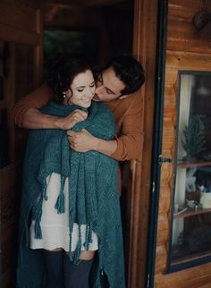 a man and woman embracing each other in front of a door with a green shawl draped over their shoulders