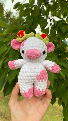 a hand holding a small white and pink crocheted cow with flowers on it's head