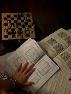 a person's hand is on top of an open book with chess pieces in the background