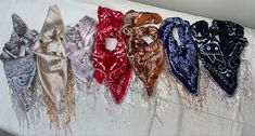 six scarves are lined up on a white tablecloth with beads and sequins