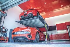 two cars are parked on top of each other in a garage with red cabinets and flooring