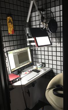 a desk with a computer monitor, keyboard and mouse next to a microphone on the wall