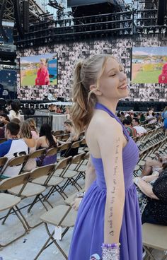 a woman in a purple dress standing next to a crowd at a baseball game with tattoos on her arm