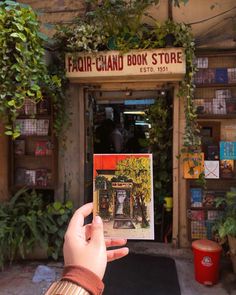 a person holding up a book in front of a building with plants growing on it