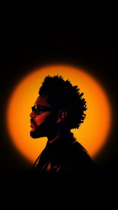 the silhouette of a man wearing glasses in front of an orange sun