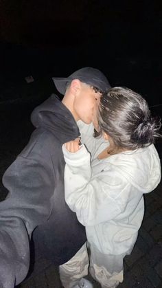 a man and woman kissing each other on the street at night with their arms around each other