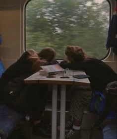 two people sitting at a table on a train looking out the window with trees in the background