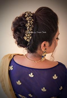 a woman wearing a blue blouse with gold jewelry on her head and hair in a bun