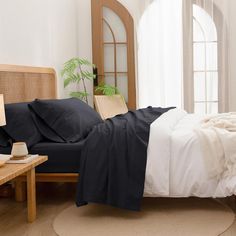 a bed with black and white sheets in a room next to a table, potted plant and window