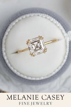 an engagement ring with a princess cut diamond in the center, sitting on top of a white plate