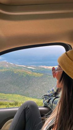 a woman sitting in the back seat of a car looking out at mountains and trees