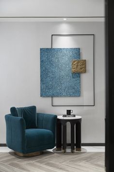 a blue chair sitting in front of a painting on the wall next to a table