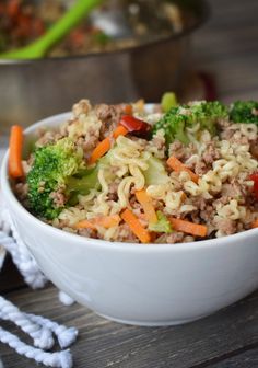 a white bowl filled with rice and vegetables on top of a wooden table next to a pot