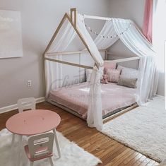 a white canopy bed sitting in a bedroom on top of a hard wood floor next to a pink table and chair