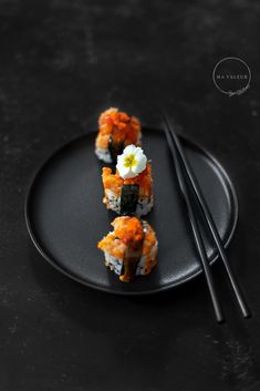 three pieces of sushi on a black plate with chopsticks and sauce in the middle