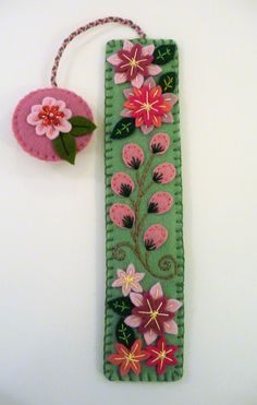 a green bookmark with pink flowers on it next to a flower brooch pin