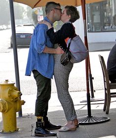 a man and woman kissing under an umbrella on the sidewalk near a yellow fire hydrant