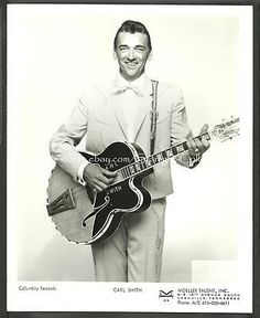 a black and white photo of a man in a suit holding a guitar with his right hand