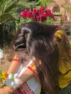 a woman with long hair holding flowers in her hand and looking down at the ground