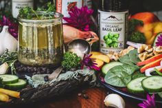 a table topped with lots of different types of vegetables and jars filled with liquid next to each other