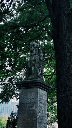 a statue in the middle of a park next to a tree