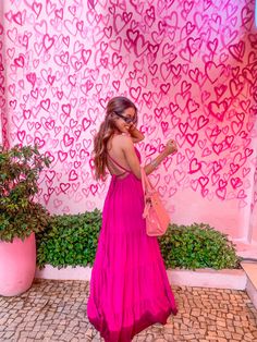 a woman standing in front of a wall with hearts painted on it and holding a pink purse