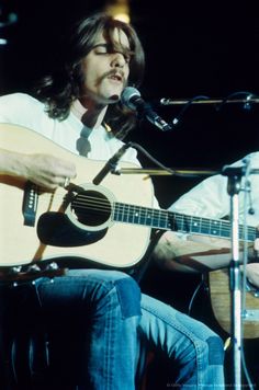 a man sitting in front of a microphone while holding a guitar and singing into a microphone