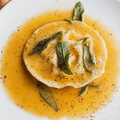 a white plate topped with food covered in sauce and garnished with green leaves