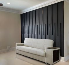 a white couch sitting in front of a wall with black paneling on the walls