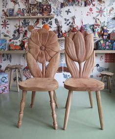 two wooden chairs sitting next to each other in front of a wall with flowers on it