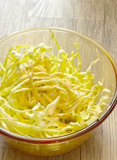 a bowl filled with shredded cabbage on top of a wooden table