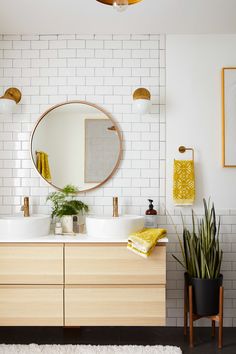 a bathroom with two sinks and a round mirror above it, along with potted plants