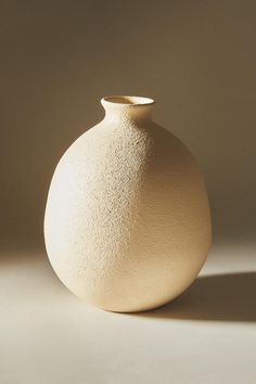 a white vase sitting on top of a table next to a wall in the shadows