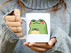 a woman holding a coffee mug with a cartoon frog on it's front and side